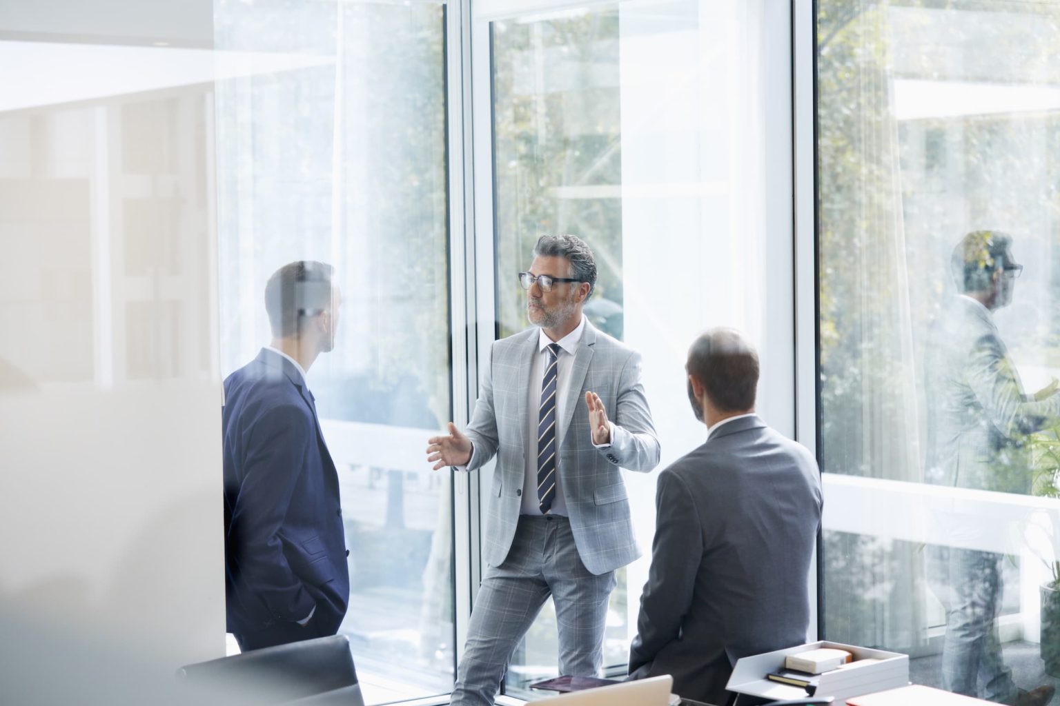 Confident businessman discussing with colleagues in meeting by window at office